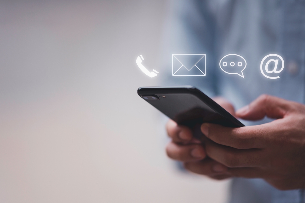 Symbolische Darstellung der Kontaktaufnahme: Hand hält Smartphone mit schwebendem @-Zeichen